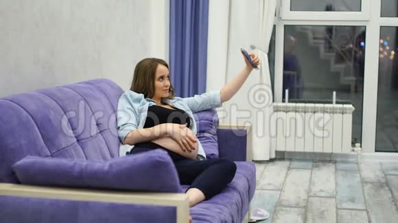 漂亮的孕妇坐在客厅的沙发上Dalet为社交网络自拍互联网之流视频的预览图