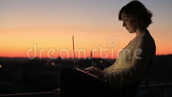 在温暖的阳光明媚的户外女人在笔记本电脑键盘上打字美丽的城市日落视频的预览图