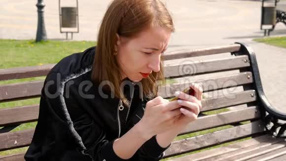 年轻漂亮的女人在公园的手机上拨一条短信大学女生短信手机侧视图视频的预览图