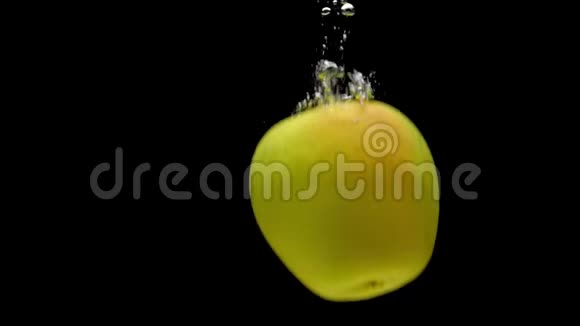 一个黄色的苹果掉进了黑色背景的透明水中视频的预览图