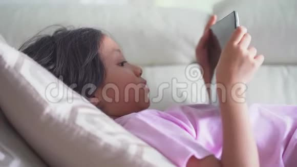 小女孩在舒适的沙发上用平板电脑视频的预览图