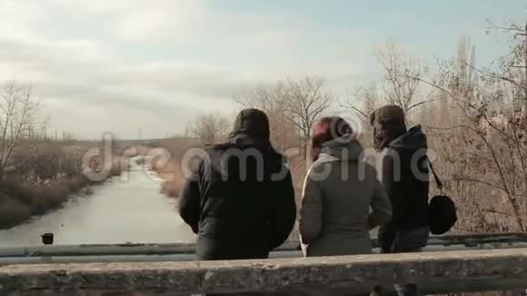 三个人站在一座桥上俯视着河寒冷的冬天视频的预览图