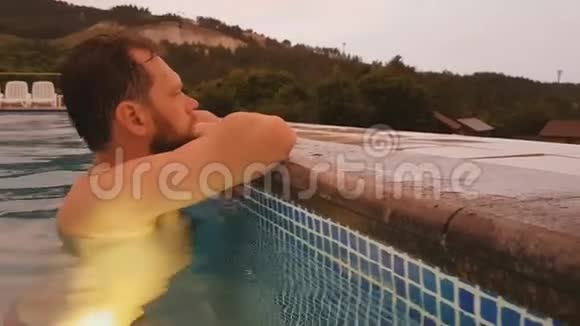 一个留胡子的人正在暑假日落时在室外游泳池游泳手机录像视频的预览图