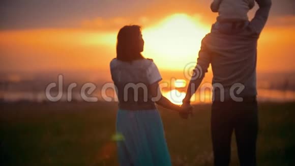 一家人走过田野欣赏日落爸爸妈妈牵着手儿子坐在肩膀上后景视频的预览图