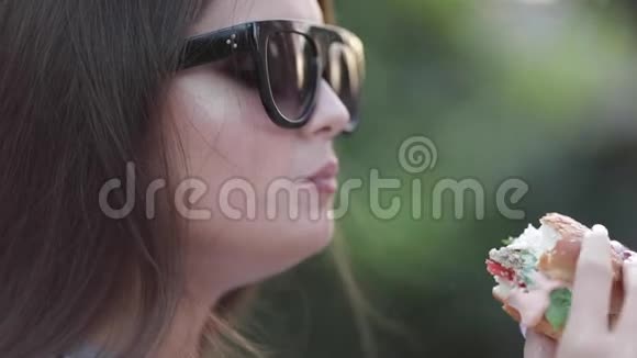 年轻女孩戴着时尚的太阳镜嘴唇明亮享受美味的汉堡视频的预览图