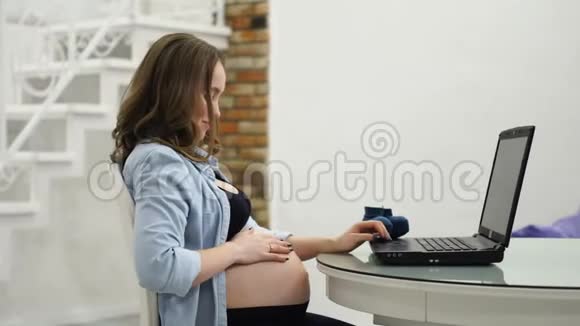 孕妇作家在休产假时坐在电脑前抚摸着一本新书的几页视频的预览图