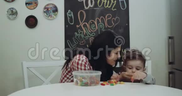 穿着睡衣的小男孩和妈妈在餐桌上的厨房里玩糖果红色史诗视频的预览图