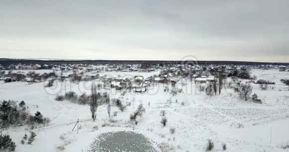 冰冻的池塘覆盖着一场雪和一个村庄附近覆盖着一场雪的植物冬季景观视频的预览图
