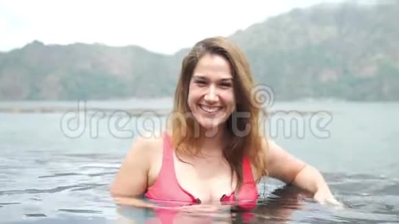 美丽的年轻女孩在游泳池里笑湖和山景视频的预览图
