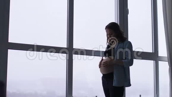 一个幸福微笑的孕妇在一个别致的公寓里的早晨有着全景的窗户一个女人在等待视频的预览图