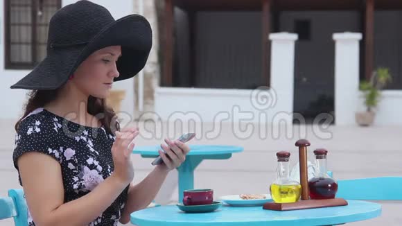 漂亮的女人坐在街边的咖啡馆里在智能手机上打字微笑着视频的预览图