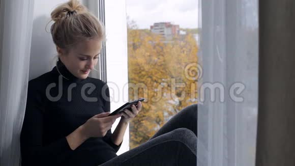 女人坐在窗台上用电子阅读器读一本书视频的预览图
