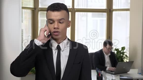 年轻成功的非洲商人在办公室里用智能手机说话男人在电脑里工作视频的预览图