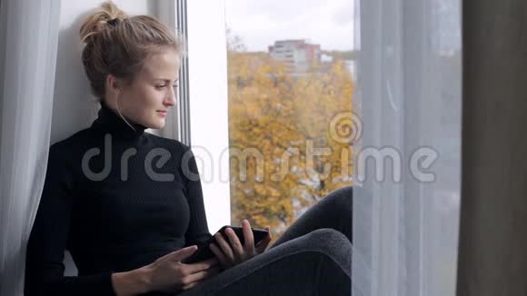 美丽的女人坐在窗台上用电子阅读器读书视频的预览图
