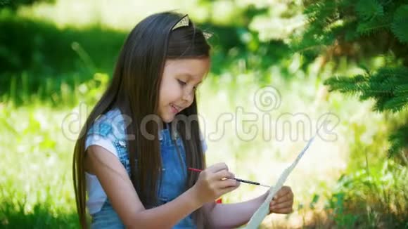 快乐的小女孩在晴天坐在草地上画水彩画视频的预览图