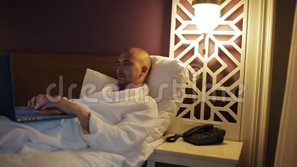 酒店内的商务人员穿着浴袍躺在床上使用笔记本电脑视频的预览图