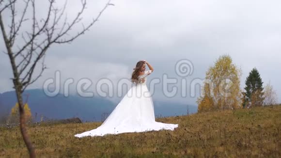 全长视野的迷人新娘穿着长长的婚纱摆姿势在秋山之巅视频的预览图