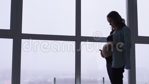 一个幸福微笑的孕妇在一个别致的公寓里的早晨有着全景的窗户一个女人在等视频的预览图