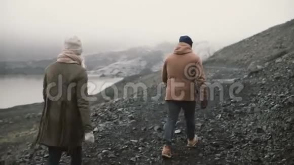 在冰湖散步的年轻夫妇的后景男人和女人一起在冰岛的山上徒步旅行视频的预览图