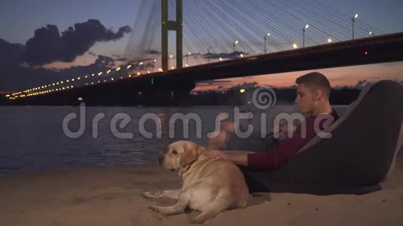 年轻人和狗坐在沙滩上抽水烟视频的预览图