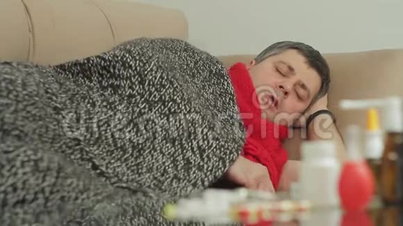一个有感冒迹象的人躺在沙发上的公寓里咳嗽得厉害视频的预览图