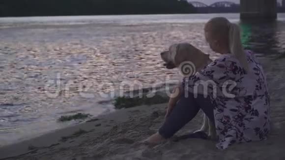 美丽的女孩和一只狗在河岸散步视频的预览图