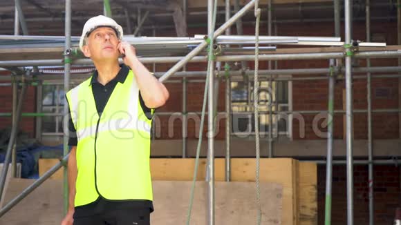 男建筑工人拿着剪贴板用手机说话视频的预览图