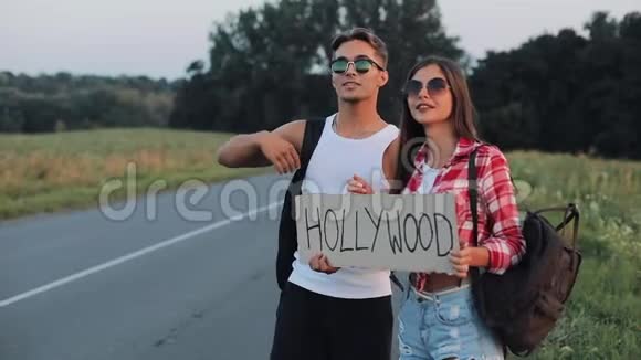 一对年轻夫妇正站在路上搭便车一男一女在高速公路上停着一个标志好莱坞视频的预览图