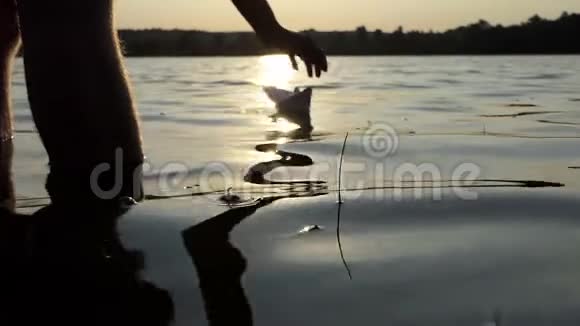可爱的纸船是一个男孩在日落时在湖里发射的视频的预览图