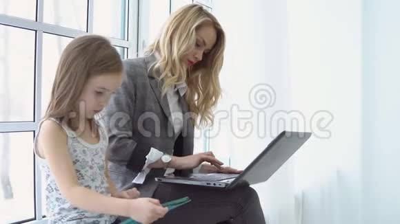 年轻的女商人和她的女儿和笔记本电脑坐在窗边视频的预览图