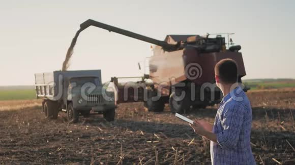 英俊的农民与平板站在联合收割机的背景农民使用现代技术触摸平板电脑视频的预览图