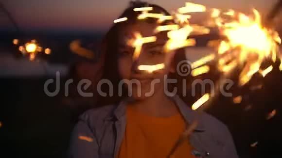 快乐的年轻女人带着火花看着相机微笑着看着夏天的日落视频的预览图