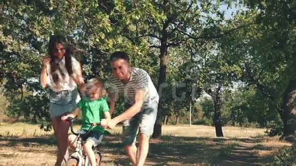 幸福的家庭母亲父亲和儿子都在大自然中行走孩子在骑自行车父母帮助他视频的预览图