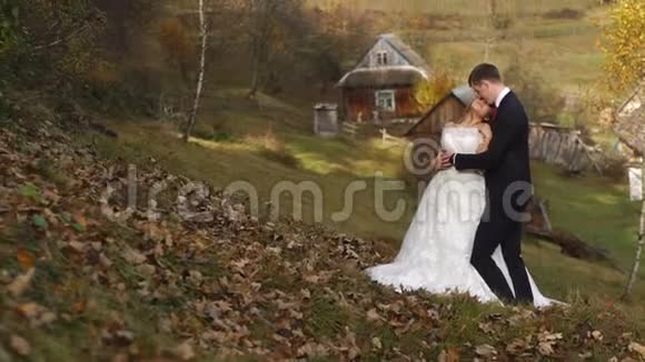 婚礼全长拍摄的年轻迷人的新婚夫妇在村里温柔地拥抱在秋天视频的预览图