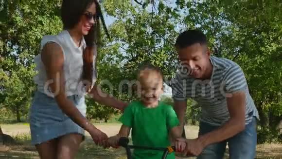 幸福的家庭母亲父亲和儿子都在大自然中行走孩子在骑自行车父母帮助他视频的预览图