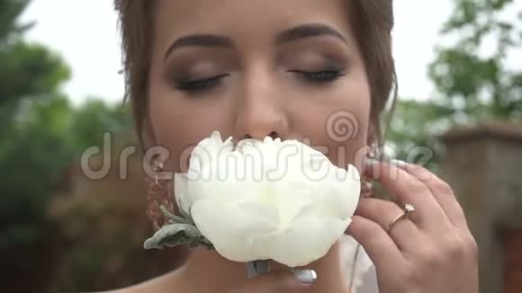 特写肖像的迷人新娘用自然的化妆用紧闭的眼睛闻着白牡丹视频的预览图