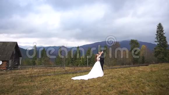 新婚夫妇温柔拥抱在山里的秋村的婚礼肖像帅哥新郎在接吻视频的预览图