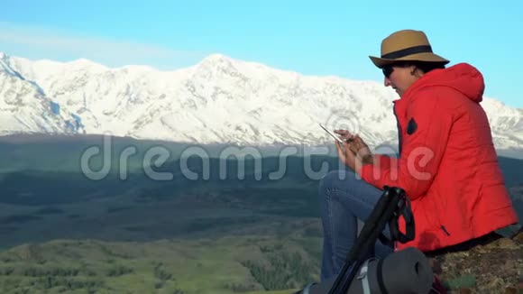 旅行者的女人坐在岩石上用智能手机拍摄雪山视频的预览图