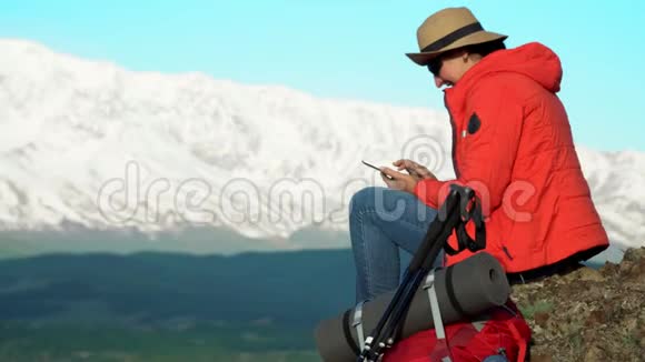 旅行者的女人坐在岩石上用智能手机拍摄雪山视频的预览图
