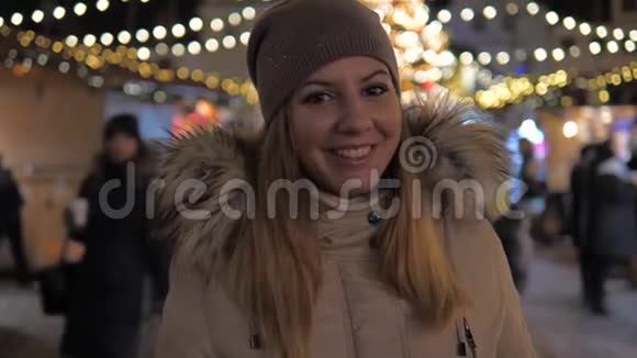 穿着温暖衣服微笑的女人站在圣诞市场上照明视频的预览图
