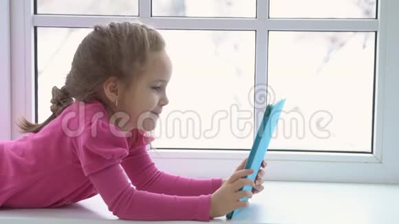 穿着粉红色连衣裙的高级女孩正拿着平板电脑坐在窗边视频的预览图