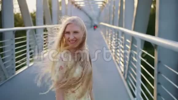 女人回头看桥漂亮的金发女郎回头看镜头一边在桥上奔跑留着波浪发视频的预览图