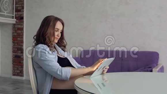 幸福的孕妇坐在玻璃餐桌旁喝咖啡用平板电脑看着家人视频的预览图