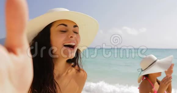 女孩手持手机欢迎女性在沙滩上自拍照夏日草帽中的快乐游客视频的预览图
