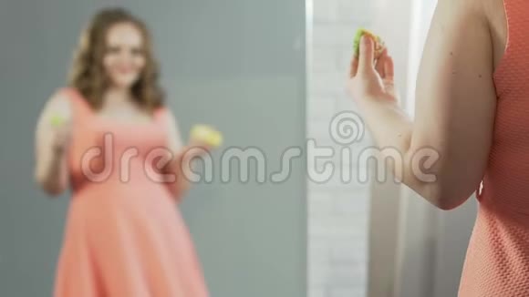 穿裙子的超重女性一边吃甜甜圈一边欣赏镜子里的倒影视频的预览图