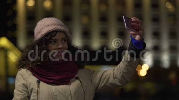 快乐的混血女孩在夜间城市背景下自拍以保存记忆视频的预览图