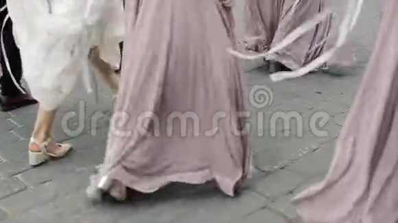 一位身着白色礼服的新娘和三位身着优雅长裙的伴娘在沥青上散步视频的预览图