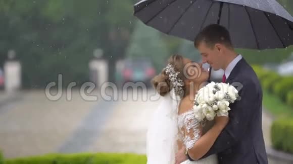 开朗时尚刚结婚的夫妇在雨中轻轻地拥抱在伞下半身像视频的预览图