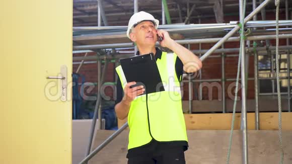 男建筑工人在建筑工地用剪贴板和手机交谈视频的预览图