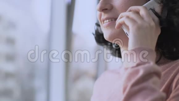 女人一边用手机聊天一边微笑一边隔着窗户视频的预览图